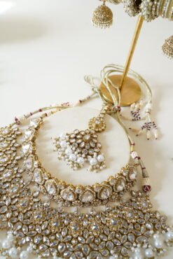 Seyora two-layer South Asian bridal necklace set featuring clear stone and pearl settings with a choker, longer necklace, matching jhumka earrings, and a maang tikka