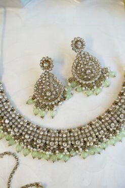 Zoya necklace set featuring clear sparkling stones, hanging pearl beads, matching drop earrings, and a maang tikka.
