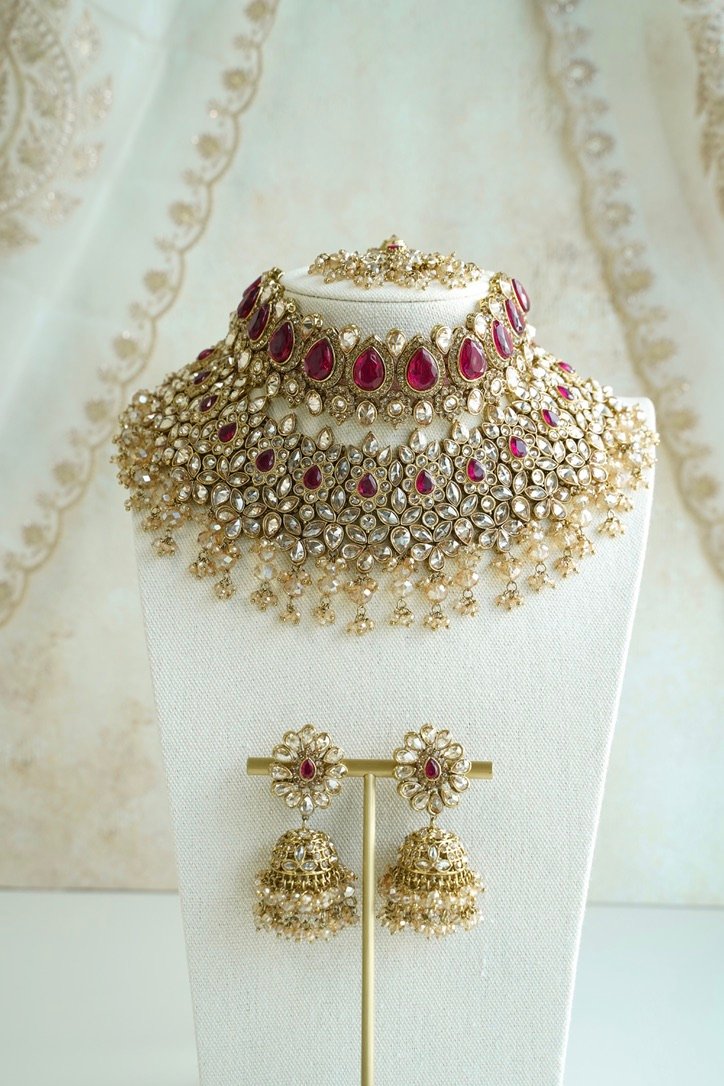 Seyora two-layer South Asian bridal necklace set featuring rani pink stone and pearl settings with a choker, longer necklace, matching jhumka earrings, and a maang tikka.