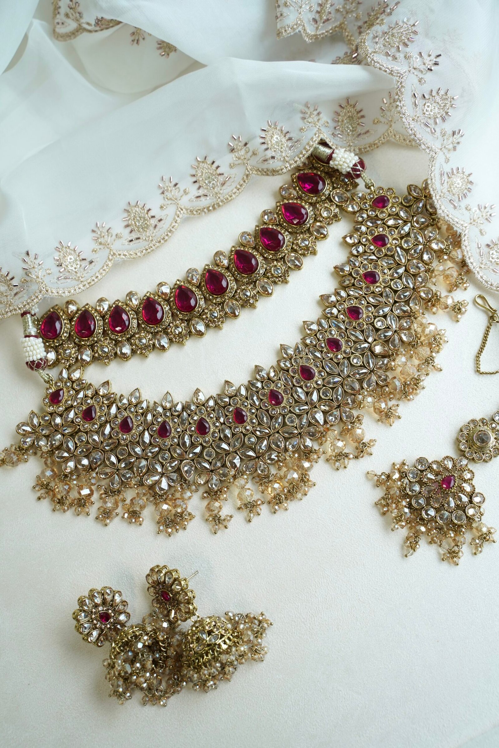 Seyora two-layer South Asian bridal necklace set featuring rani pink stone and pearl settings with a choker, longer necklace, matching jhumka earrings, and a maang tikka.