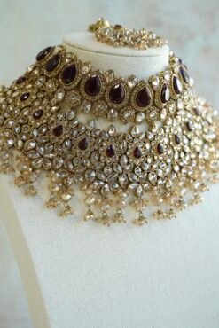Seyora two-layer South Asian bridal necklace set featuring maroon stone and crystal bead settings with a choker, longer necklace, matching jhumka earrings, and a maang tikka