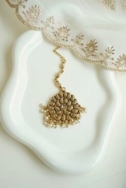 Detailed close-up of a circular antique gold maang tikka with a central crystal stone and hanging delicate white pearl clusters.