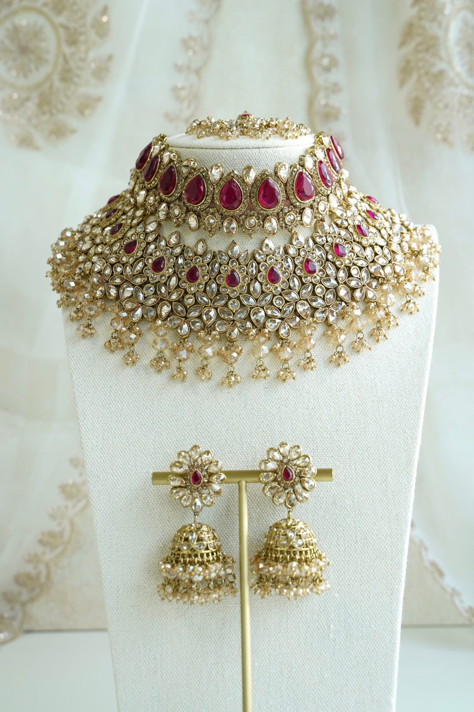 Seyora two-layer South Asian bridal necklace set featuring rani pink stone and pearl settings with a choker, longer necklace, matching jhumka earrings, and a maang tikka.