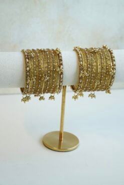 A complete stack of golden kashmiri glass bangles paired with hanging gold ghungroo charms and thin border kadas on each end from Seyora Jewels.