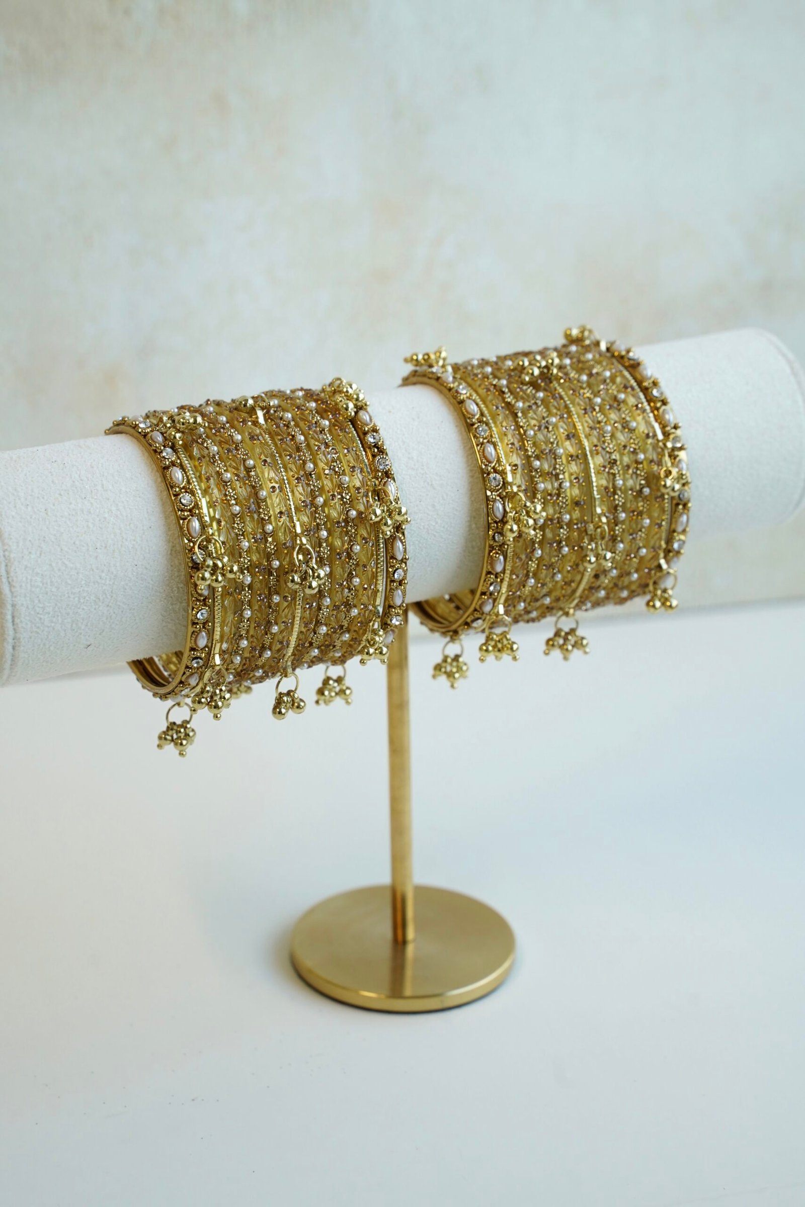 A complete stack of golden kashmiri glass bangles paired with hanging gold ghungroo charms and thin border kadas on each end from Seyora Jewels.