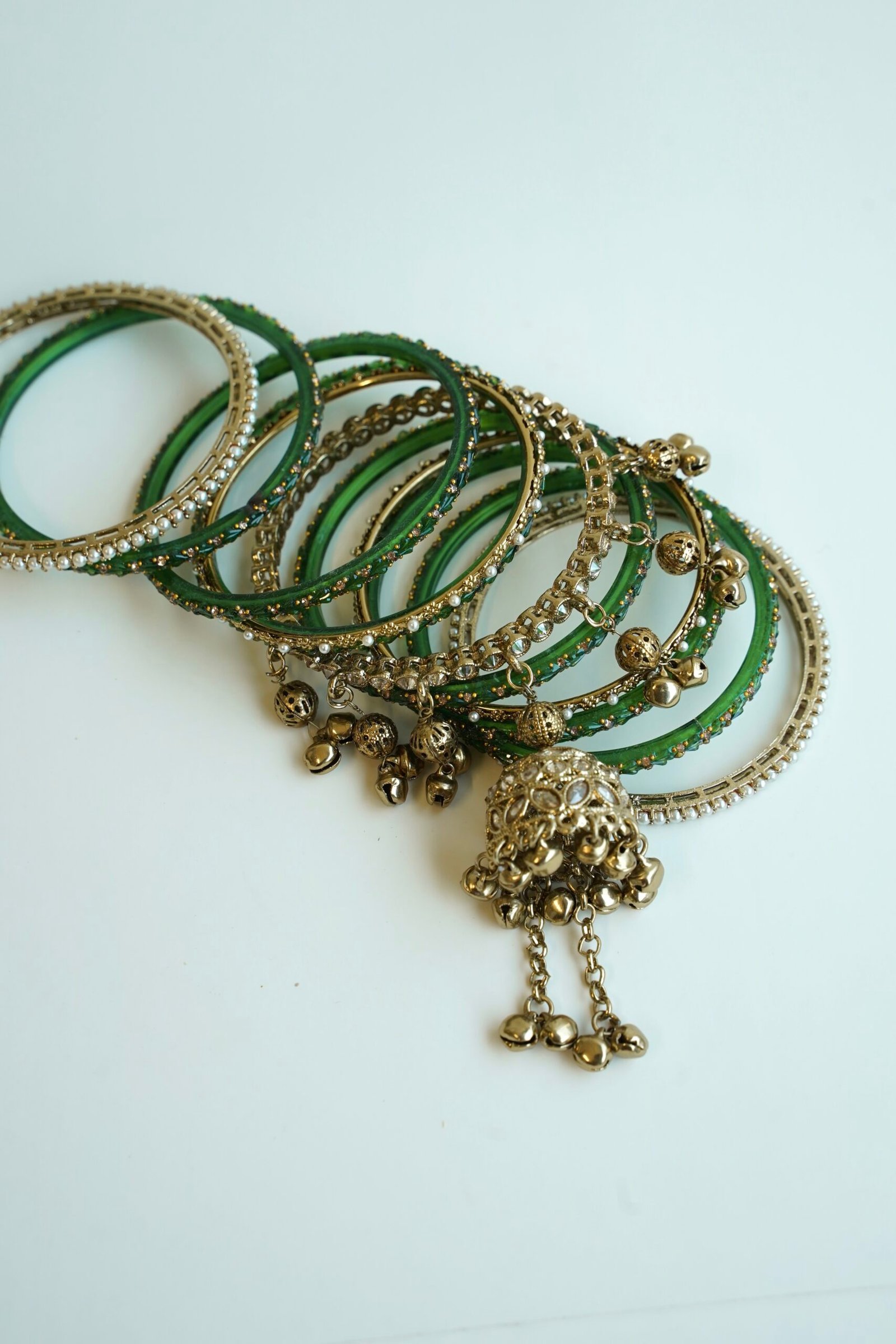 A stack of traditional South Asian glass bangles featuring a prominent central gold jhumka bangle adorned with hanging musical ghungroo beads by Seyora Jewels.