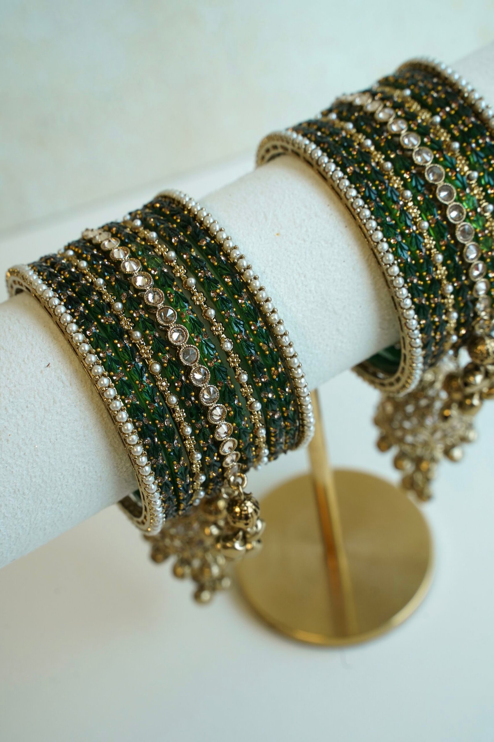 A stack of traditional South Asian glass bangles featuring a prominent central gold jhumka bangle adorned with hanging musical ghungroo beads by Seyora Jewels.