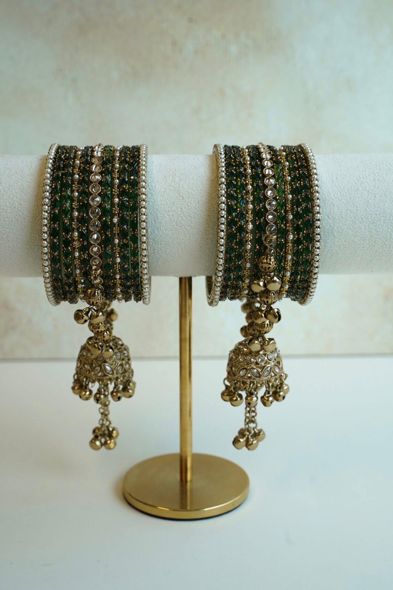 A stack of traditional South Asian glass bangles featuring a prominent central gold jhumka bangle adorned with hanging musical ghungroo beads by Seyora Jewels.