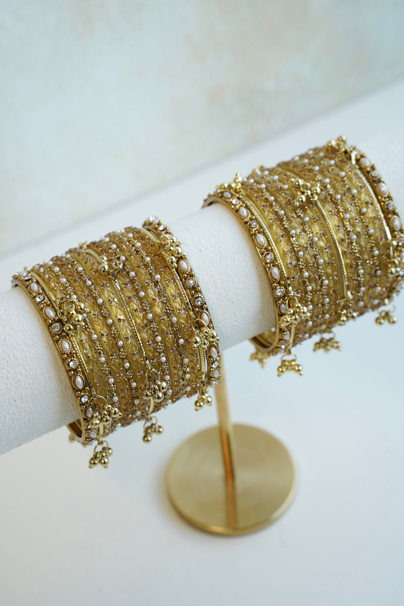 A complete stack of golden kashmiri glass bangles paired with hanging gold ghungroo charms and thin border kadas on each end from Seyora Jewels.