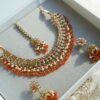 Heer necklace set in orange with antique gold necklace, pearl and orange bead drops, jhumka earrings and tikka displayed in a gift box