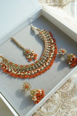 Heer necklace set in orange with antique gold necklace, pearl and orange bead drops, jhumka earrings and tikka displayed in a gift box