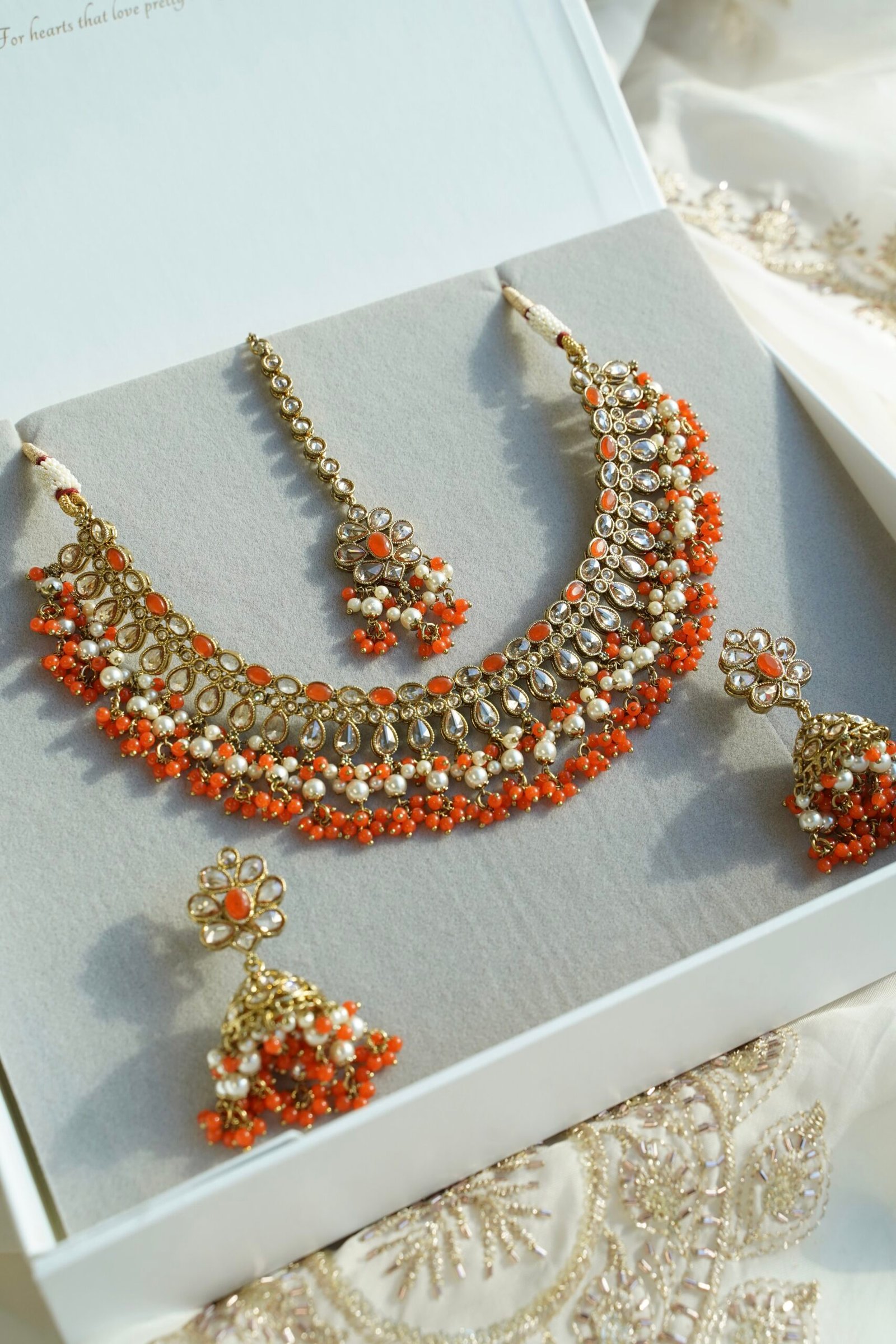 Heer necklace set in orange with antique gold necklace, pearl and orange bead drops, jhumka earrings and tikka displayed in a gift box