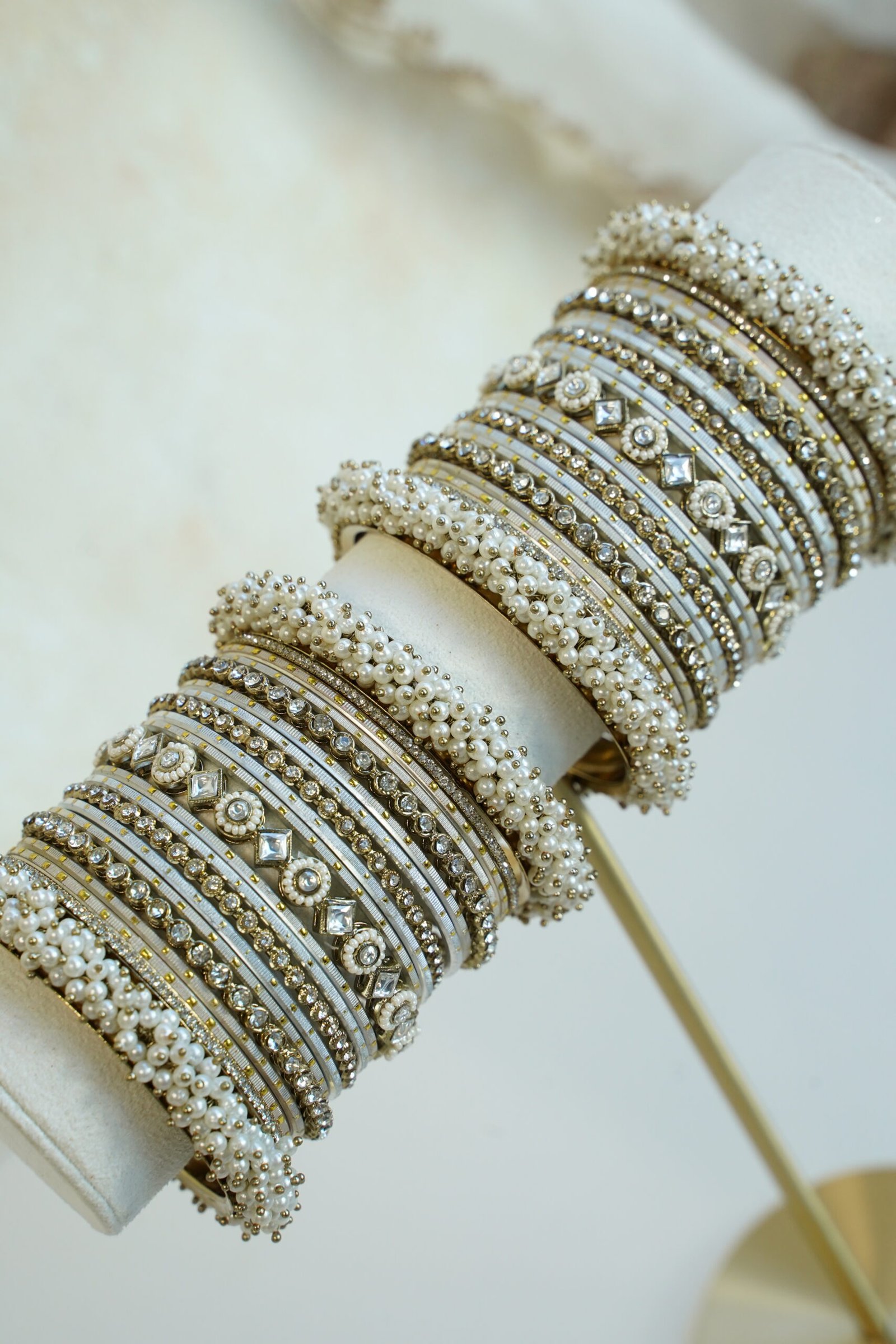 Creame bangle set with gold-tone detailing, clear stones and pearl-style bead edges stacked on a display stand