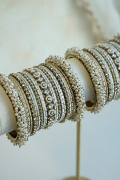 Creame bangle set with gold-tone detailing, clear stones and pearl-style bead edges stacked on a display stand