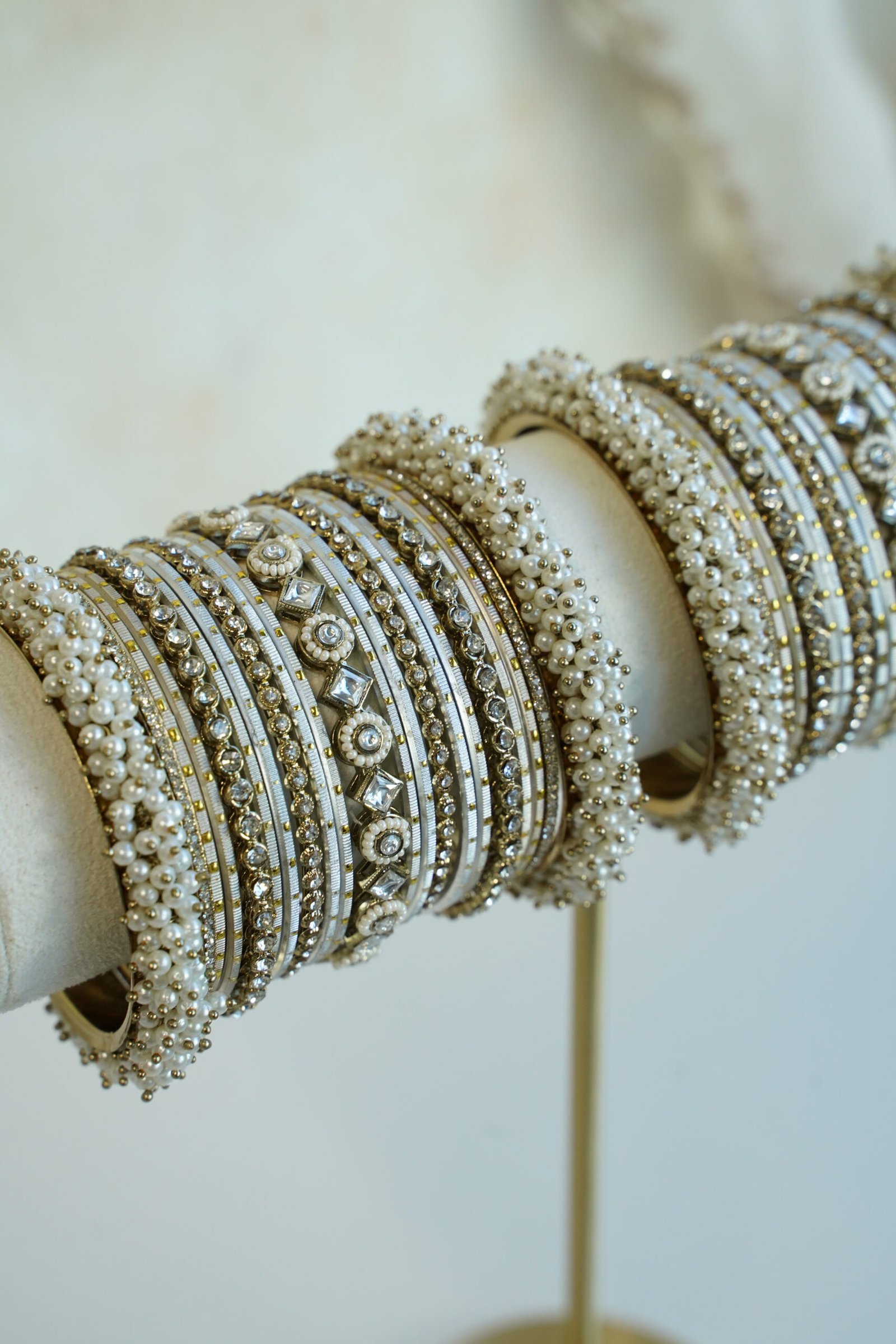 Creame bangle set with gold-tone detailing, clear stones and pearl-style bead edges stacked on a display stand