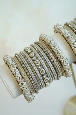 Creame bangle set with gold-tone detailing, clear stones and pearl-style bead edges stacked on a display stand