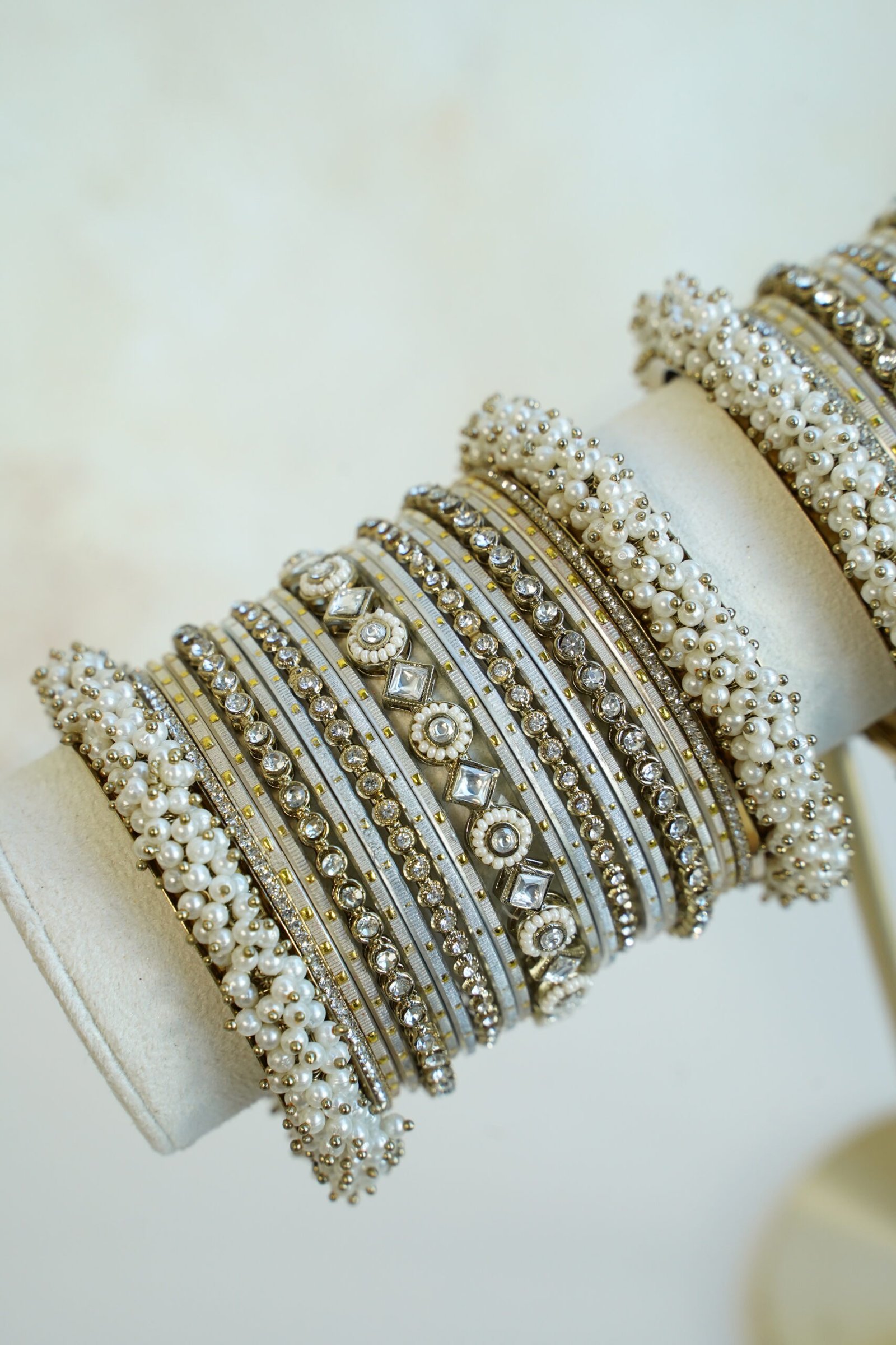 Creame bangle set with gold-tone detailing, clear stones and pearl-style bead edges stacked on a display stand