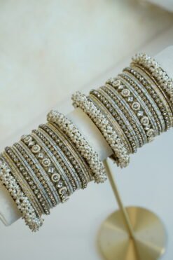 Creame bangle set with gold-tone detailing, clear stones and pearl-style bead edges stacked on a display stand