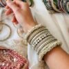 Creame bangle set with gold-tone detailing, clear stones and pearl-style bead edges stacked on a display stand