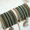 Emerald green jhumka bangle set with thread-wrapped green bangles, stone bangles, pearl-style edge bangles, and jhumka charms on a display stand