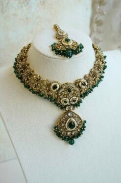 Mehr necklace set in green with antique gold-tone paisley necklace, green teardrop stones, pearl-style beads, matching earrings, and tikka on a display bust