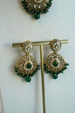 Mehr necklace set in green with antique gold-tone paisley necklace, green teardrop stones, pearl-style beads, matching earrings, and tikka on a display bust