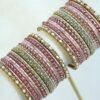 Mishti pink bangle set with thread-wrapped pink bangles, blush bands, and gold-tone edge bangles with ivory beads and clear stones on a display stand