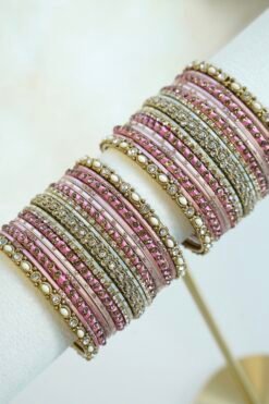 Mishti pink bangle set with thread-wrapped pink bangles, blush bands, and gold-tone edge bangles with ivory beads and clear stones on a display stand