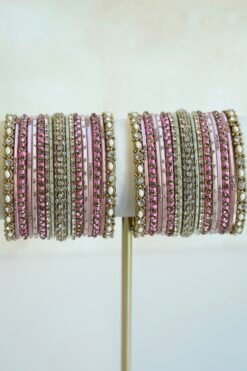 Mishti pink bangle set with thread-wrapped pink bangles, blush bands, and gold-tone edge bangles with ivory beads and clear stones on a display stand