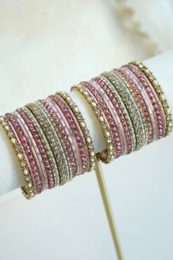 Mishti pink bangle set with thread-wrapped pink bangles, blush bands, and gold-tone edge bangles with ivory beads and clear stones on a display stand