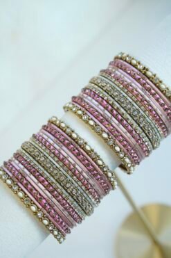 Mishti pink bangle set with thread-wrapped pink bangles, blush bands, and gold-tone edge bangles with ivory beads and clear stones on a display stand