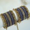 Royal blue thread and ghungroo bangle set with blue thread-wrapped bangles, champagne and clear stones, and antique gold-tone edge bangles with ghungroo charms on a display stand