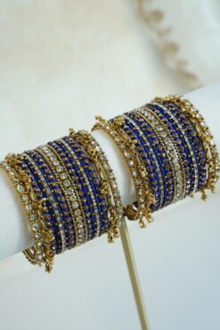 Royal blue thread and ghungroo bangle set with blue thread-wrapped bangles, champagne and clear stones, and antique gold-tone edge bangles with ghungroo charms on a display stand