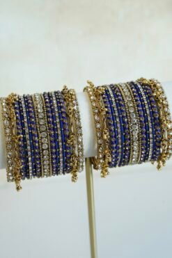 Royal blue thread and ghungroo bangle set with blue thread-wrapped bangles, champagne and clear stones, and antique gold-tone edge bangles with ghungroo charms on a display stand