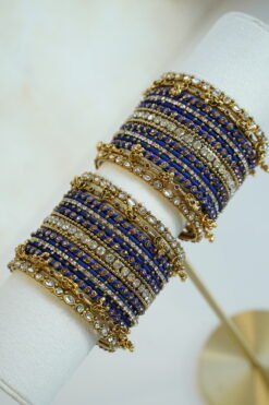 Royal blue thread and ghungroo bangle set with blue thread-wrapped bangles, champagne and clear stones, and antique gold-tone edge bangles with ghungroo charms on a display stand