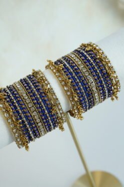 Royal blue thread and ghungroo bangle set with blue thread-wrapped bangles, champagne and clear stones, and antique gold-tone edge bangles with ghungroo charms on a display stand