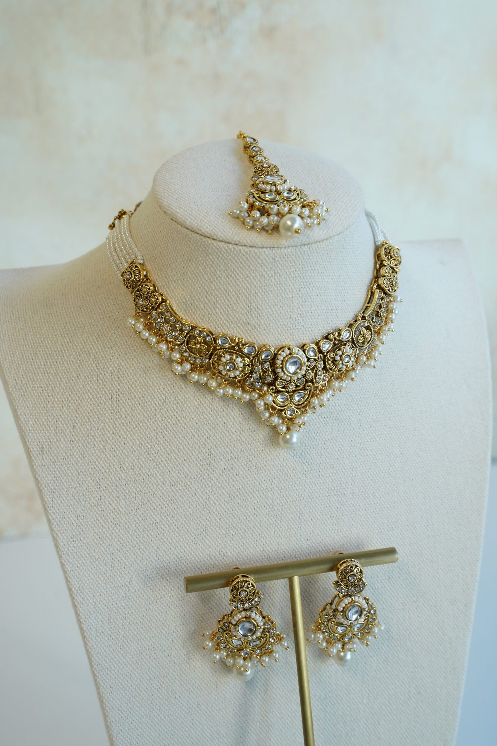 Somya white beaded artificial kundan set with antique gold necklace, pearl-style beads and clear stones, matching earrings and tikka displayed on a bust