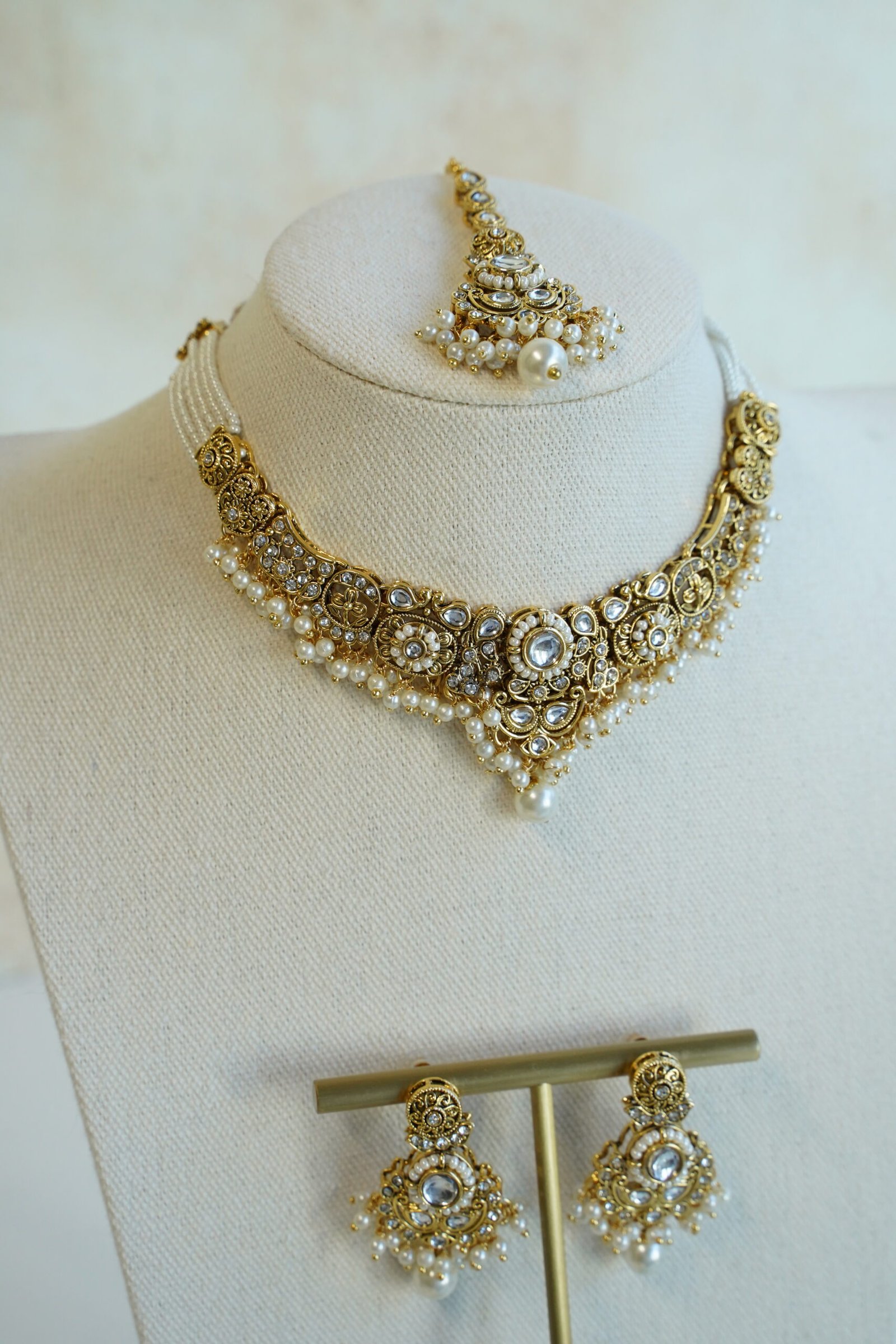 Somya white beaded artificial kundan set with antique gold necklace, pearl-style beads and clear stones, matching earrings and tikka displayed on a bust