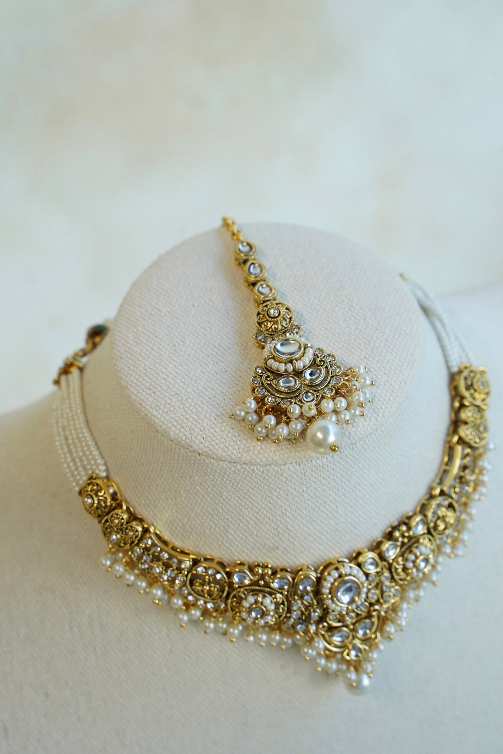 Somya white beaded artificial kundan set with antique gold necklace, pearl-style beads and clear stones, matching earrings and tikka displayed on a bust
