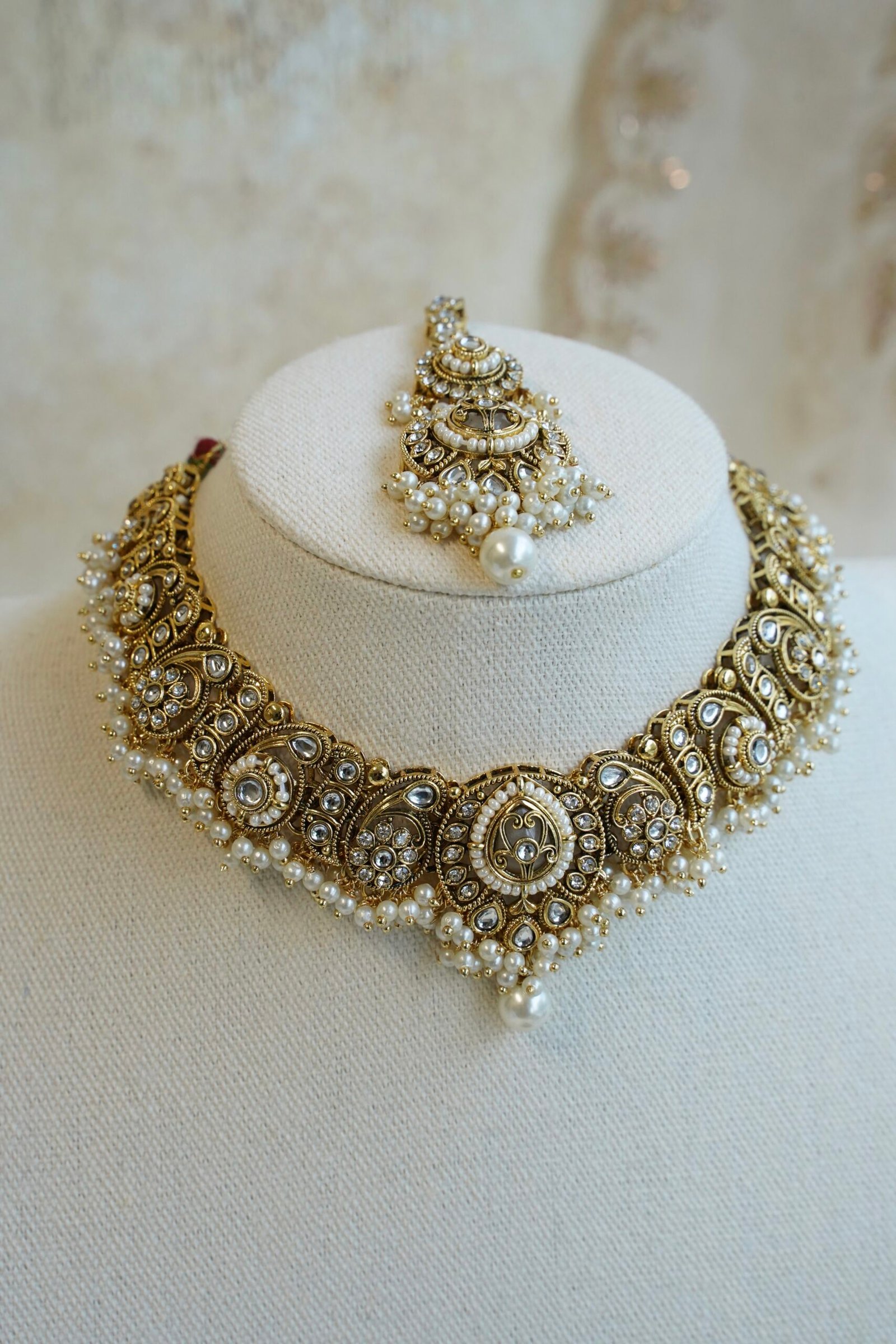 Urvi artificial kundan set with antique gold tone necklace, pearl-style bead fringe, matching earrings and tikka displayed on a bust